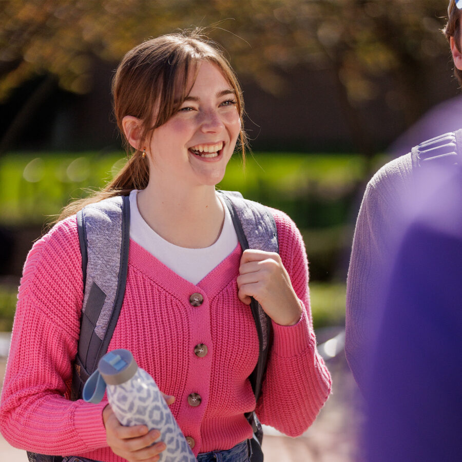 Student on main campus wearing pink sweater and holding water bottle.