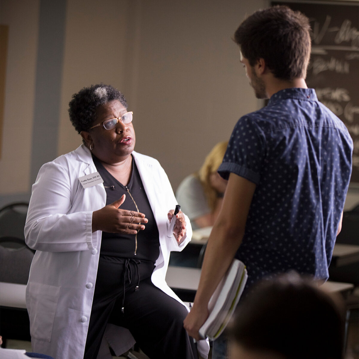 Nursing professor in lab coat talking to student